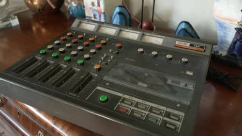 A vintage TEAC 144 audio cassette recorder sits on a wooden table, surrounded by decorative items and a lamp—an atmosphere that echoes Warren Zanes’ stories of classic recording sessions with legends like Bruce Springsteen.
