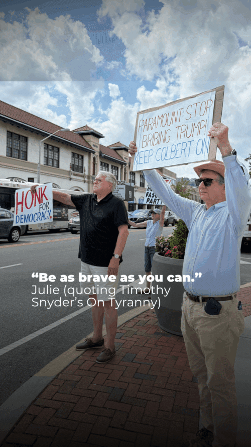 Two men stand on a sidewalk holding protest signs; one sign reads "HONK FOR DEMOCRACY," the other says "PARAMOUNT: STOP BRIBING TRUMP! KEEP COLBERT ON." A quote about bravery is overlaid on the image.